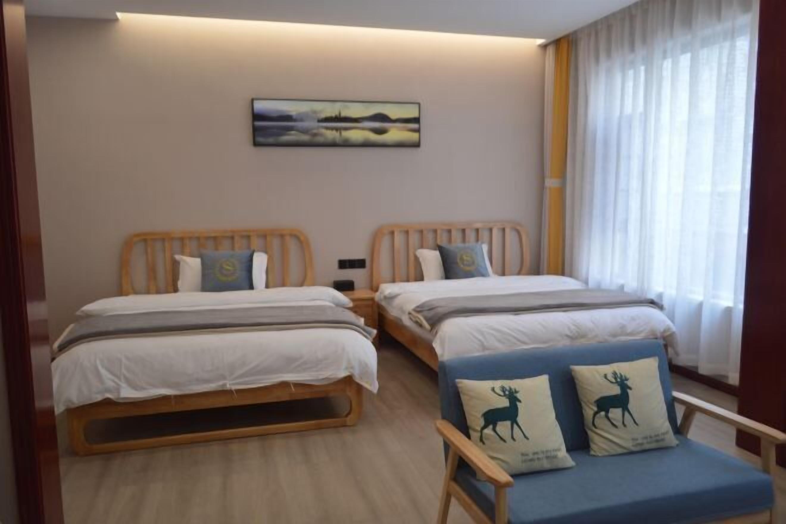 Una habitación con dos camas de madera, una silla azul con almohadones de motivos animales, un cuadro en la pared y una ventana con cortinas.