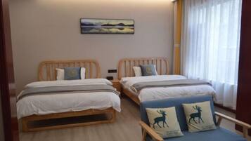 Una habitación con dos camas de madera, una silla azul con almohadones de motivos animales, un cuadro en la pared y una ventana con cortinas.