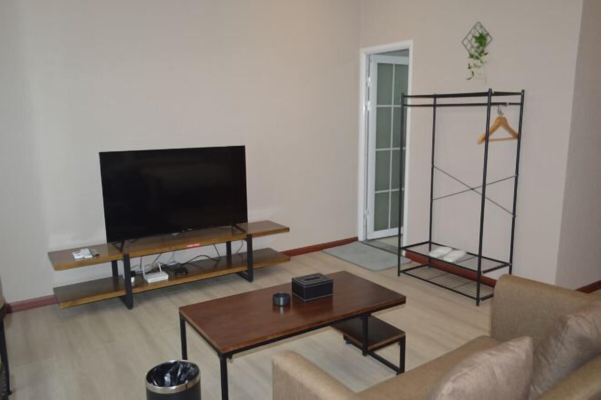 A living room with a flat-screen TV on a wooden stand, a coffee table, a sofa, and a metal clothes rack with a wooden hanger.