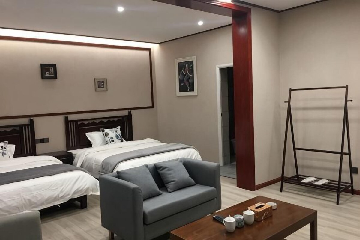 Une chambre d’hôtel avec deux lits, un canapé, une table en bois et un porte-manteau.