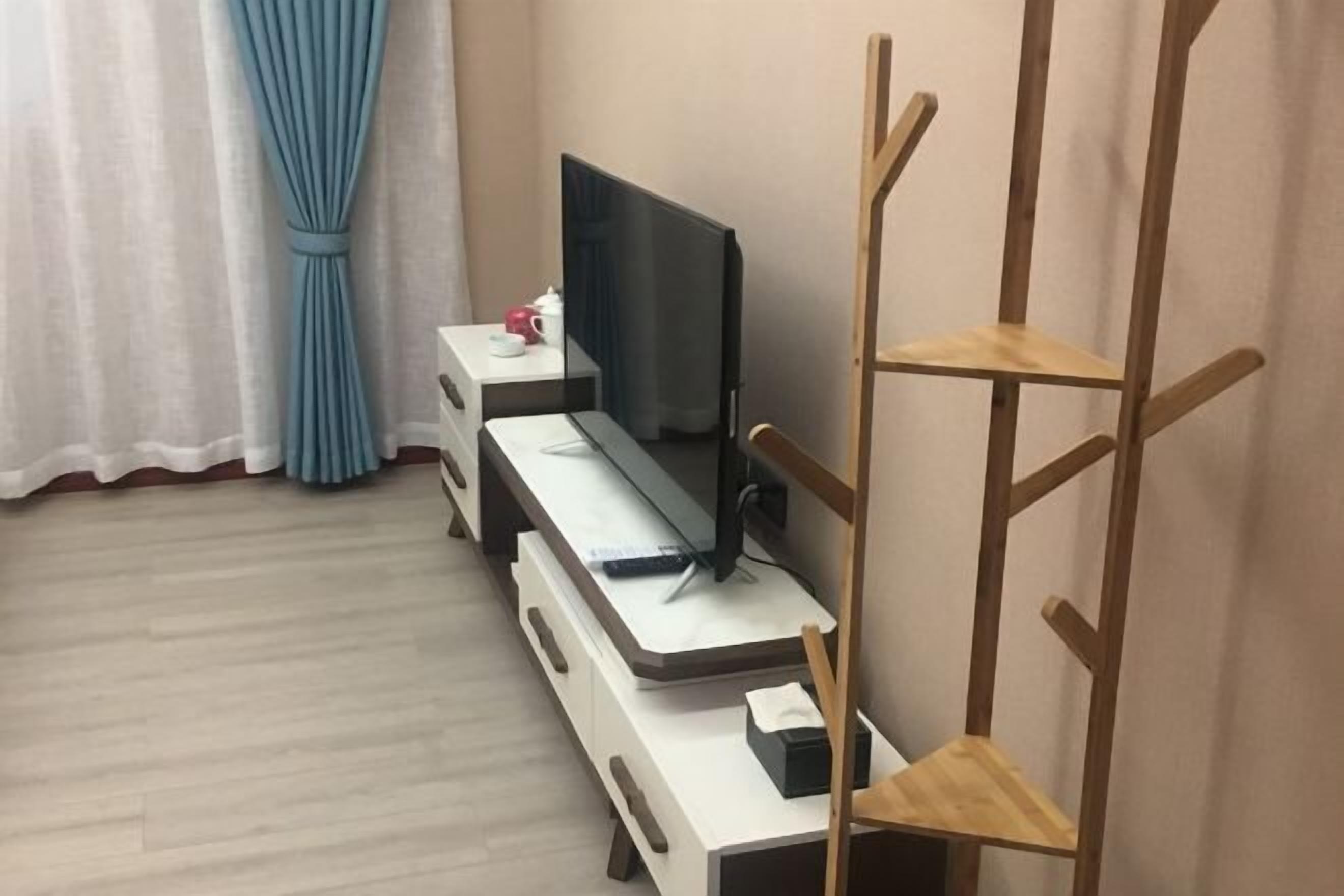 A room with a desk, a television, a wooden chair, and a curtain.