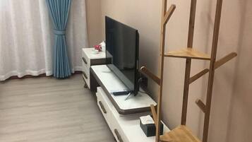 A room with a desk, a television, a wooden chair, and a curtain.