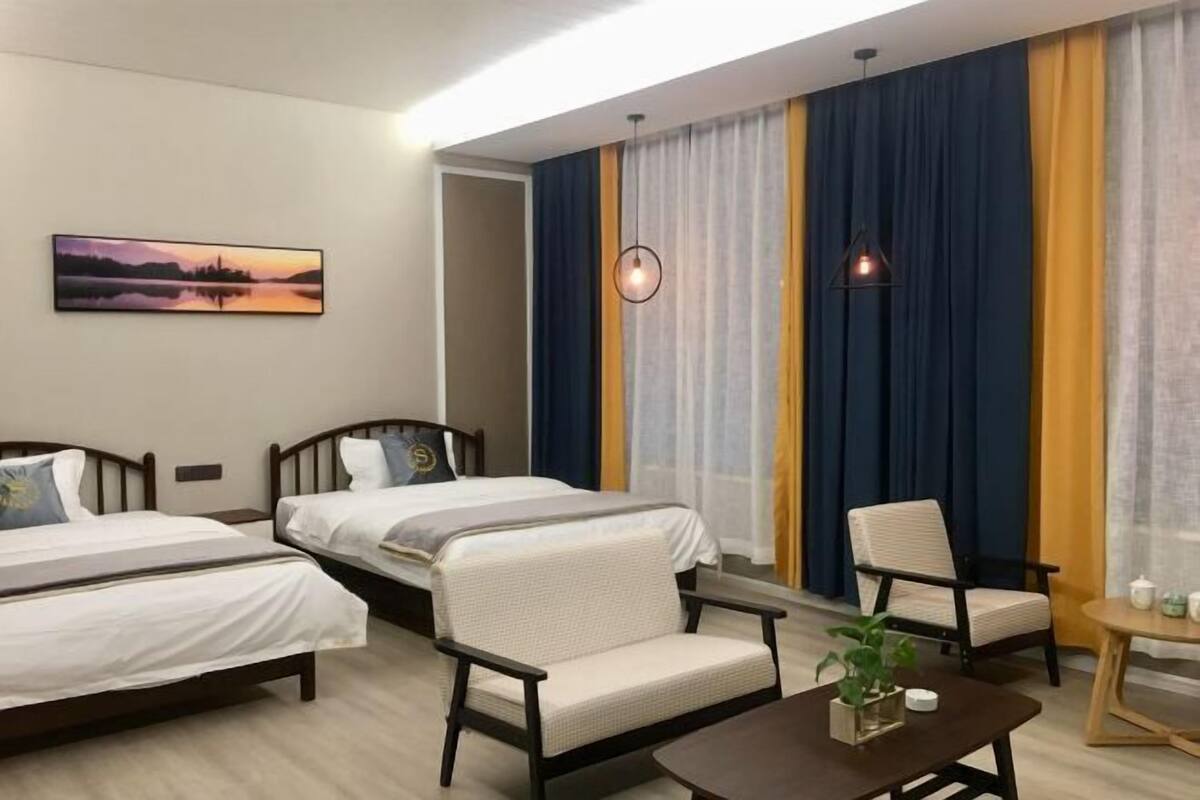 A hotel room with two beds, a chair, a small table, and a painting on the wall.