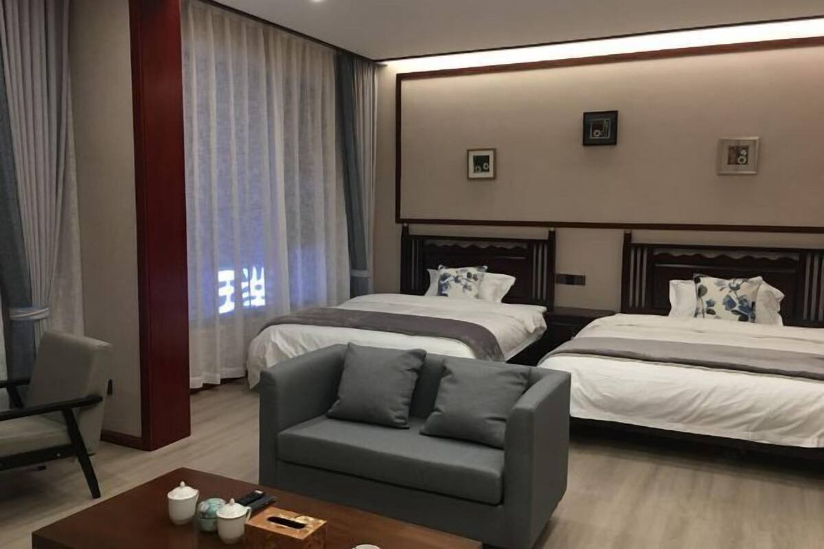 A hotel room with two beds, a sofa, a coffee table, and a large window with curtains.