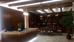 A reception area with a wooden reception desk, multiple chairs, a large potted plant, and a bookshelf filled with books and decorative items. - Puxin Inn (Dali City)