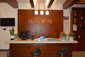 A reception desk with a wooden backdrop, a flat-screen TV, and a potted plant. - Puxin Inn (Dali City)