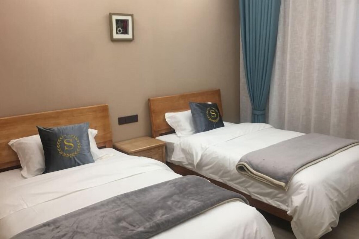 Two single beds with wooden headboards, white bedding, and a small bedside table with a lamp.