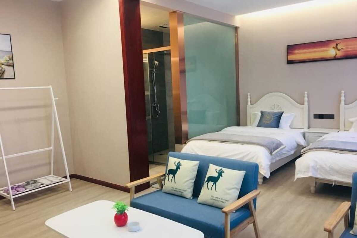 A hotel room with two beds, a sofa, a small table, a shower area, and a painting on the wall.