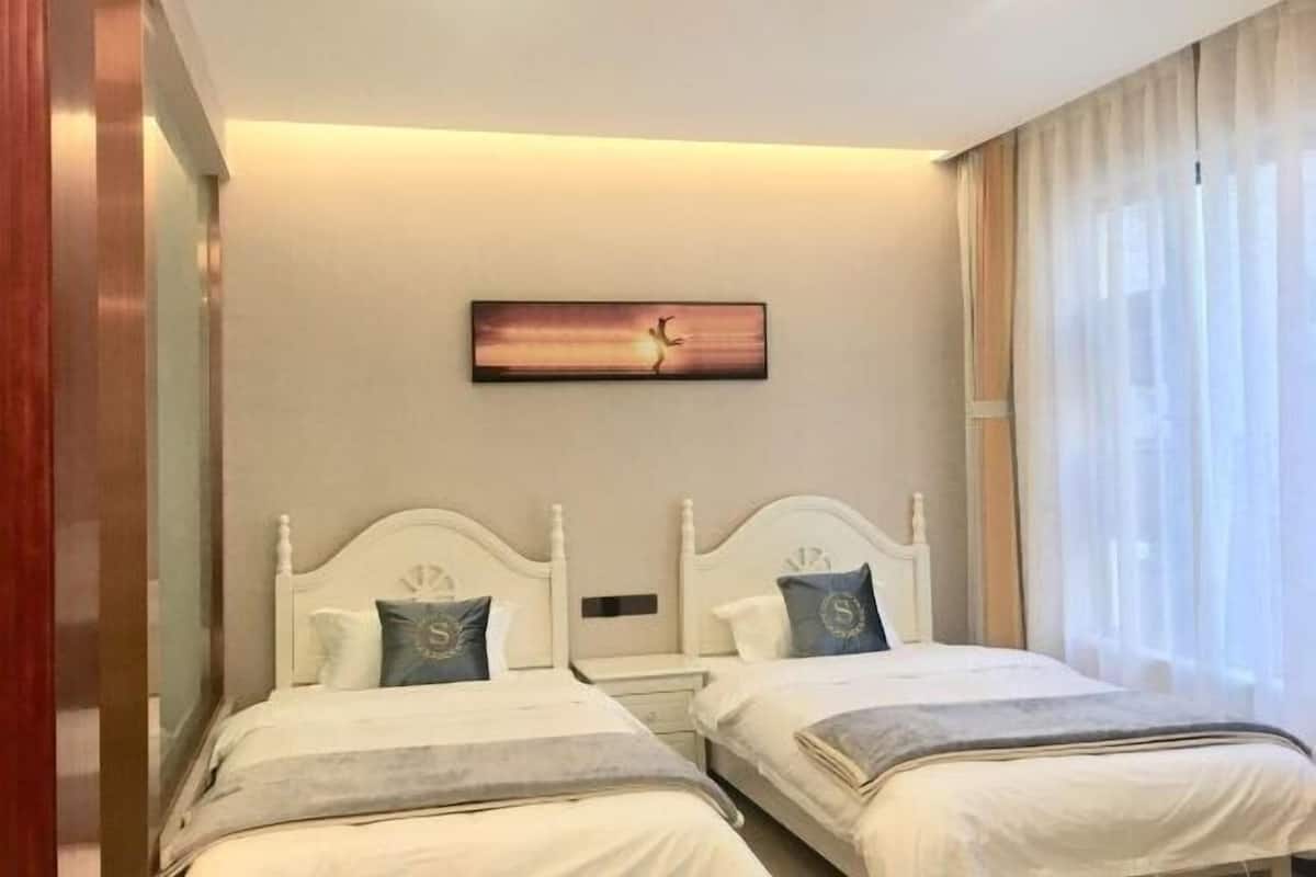 A hotel room with two beds, a painting on the wall, and a window with curtains.
