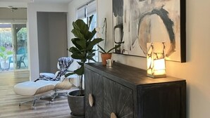 Ein modernes Wohnzimmer mit einem dunklen Holzkonsole, einem großen abstrakten Gemälde, einer Topfpflanze und einer Stehlampe.
