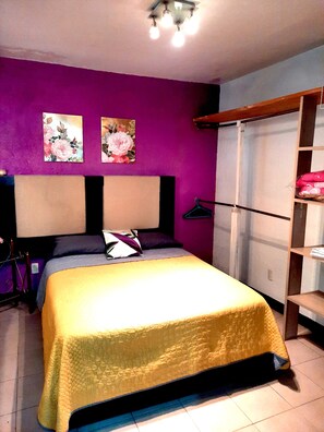 A bedroom with a bed, a wardrobe, and two floral paintings on the wall.