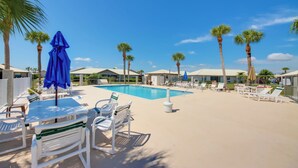 Uma área à beira da piscina com espreguiçadeiras, uma mesa e guarda-sóis.