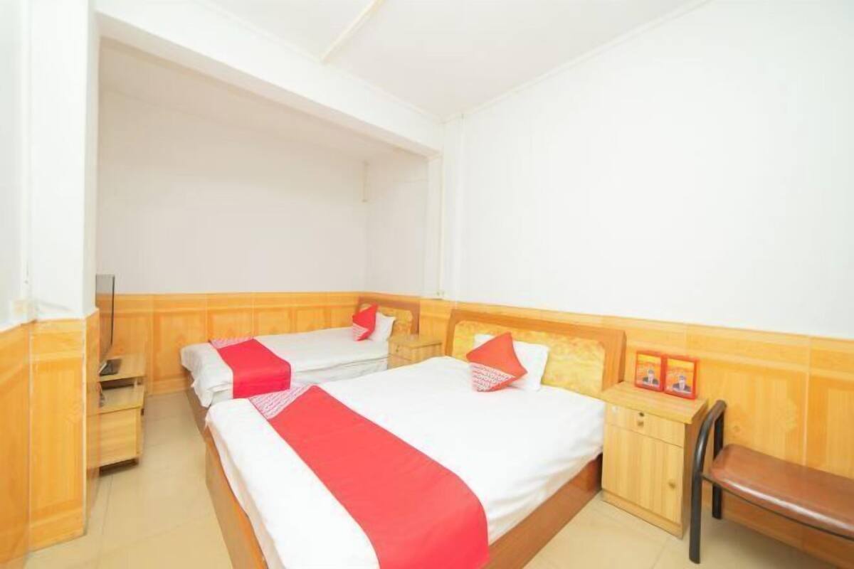A hotel room with two beds, wooden headboards, a wooden nightstand, a bench, and a small cabinet.
