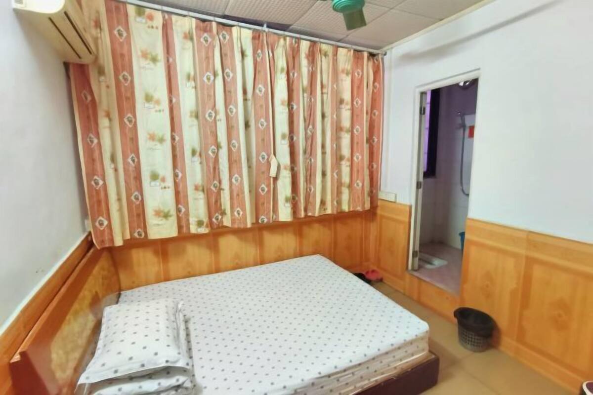 A room with a bed, wooden paneling, a curtain with a floral pattern, and a door leading to a bathroom.
