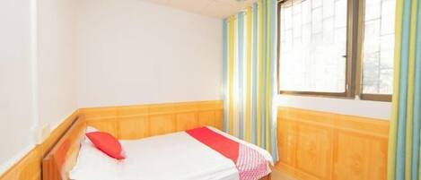 A single bed with a wooden headboard, a ceiling fan, and a window with striped curtains.