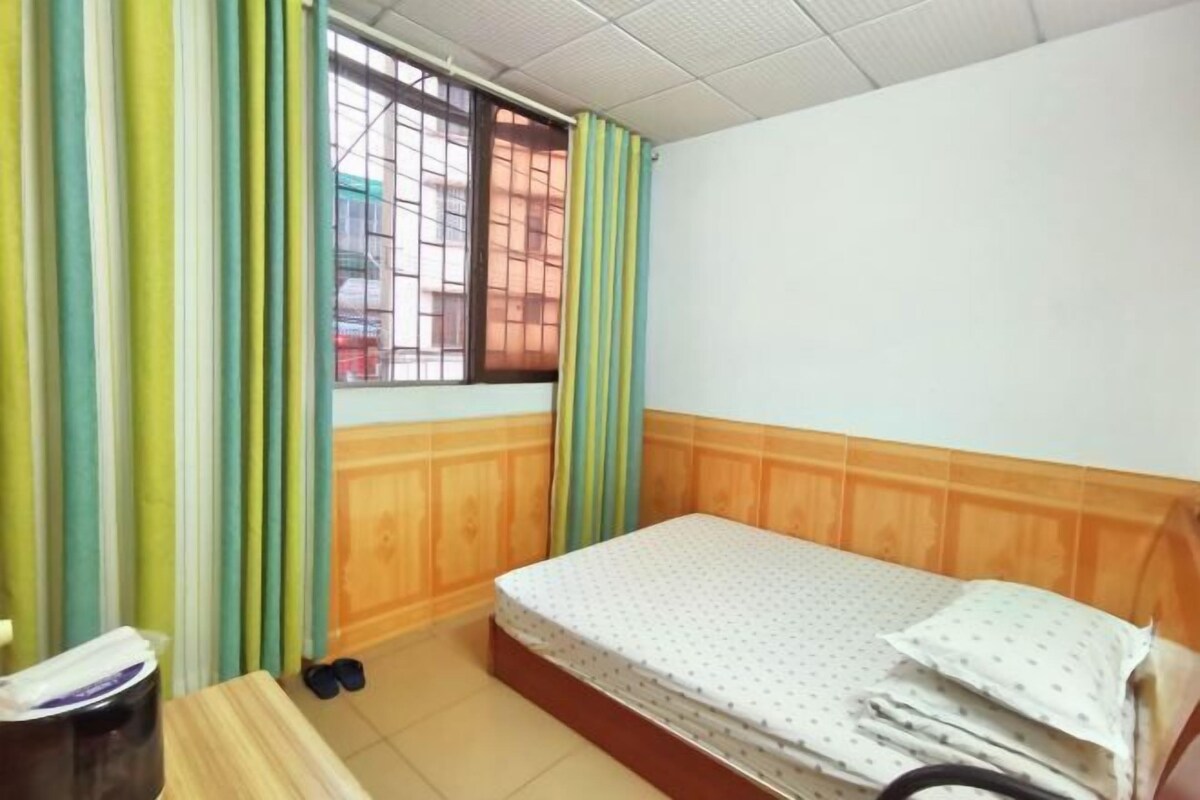 Habitació petita i senzilla amb un llit individual, una finestra amb reixetes i un capçal de llit de fusta.