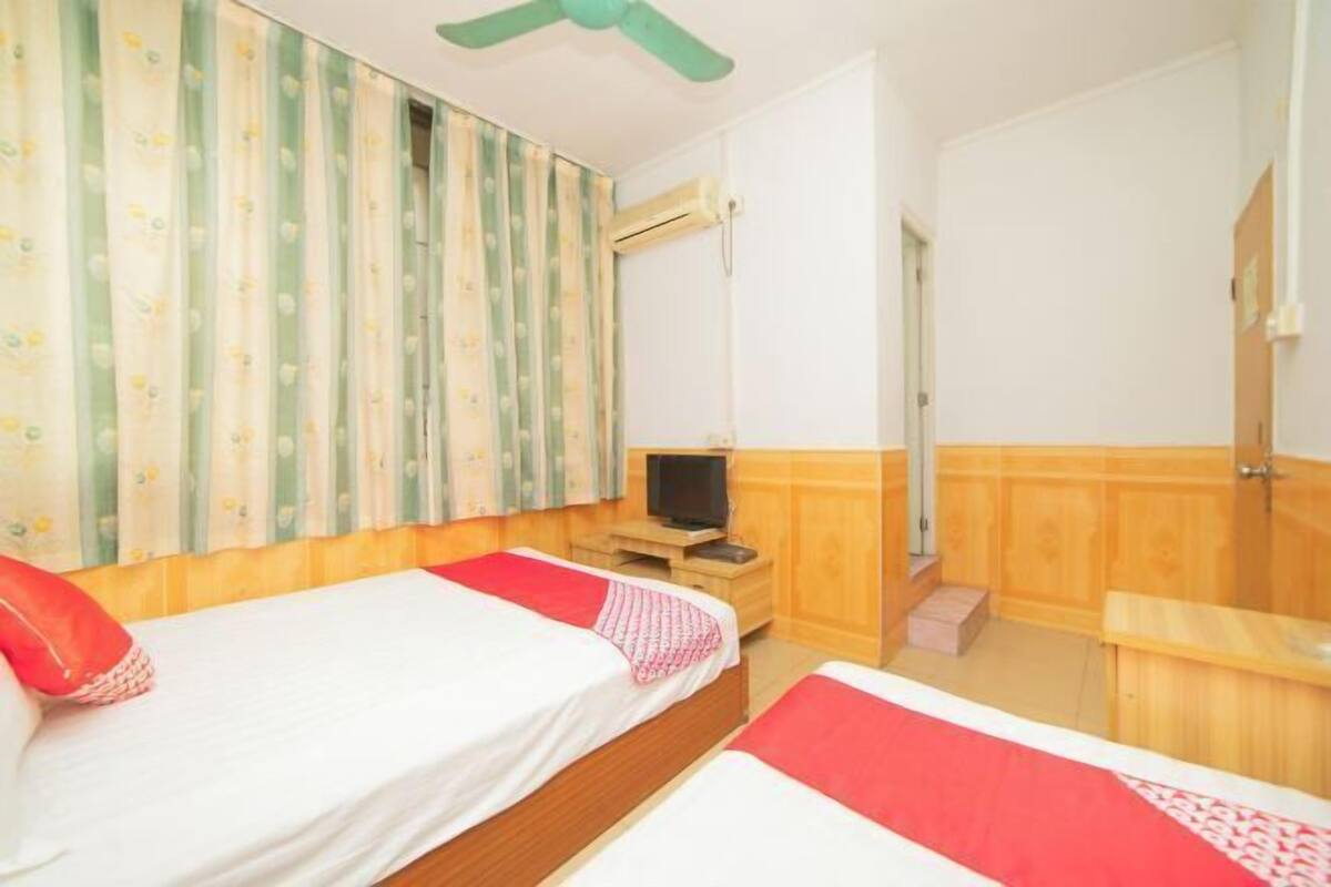 A hotel room with two beds, a TV, a wooden bench, and a window with curtains.