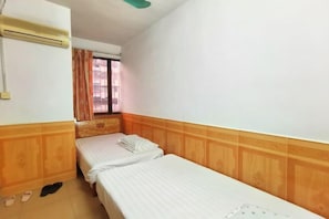 Habitació amb dos llits individuals, panells de fusta, una finestra amb cortines i un aparell d'aire condicionat.