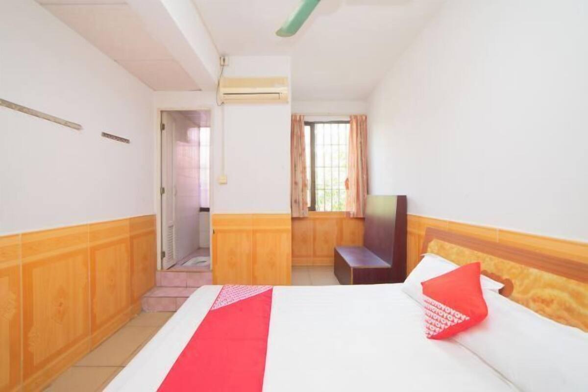 A hotel room with a bed, a wooden bench, a TV, and a window with curtains.