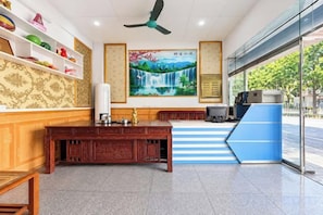A reception area with a desk, shelves, a painting, and a view through the glass door. - Xinwang · City Boutique PLUS Hotel (Jiangmen)