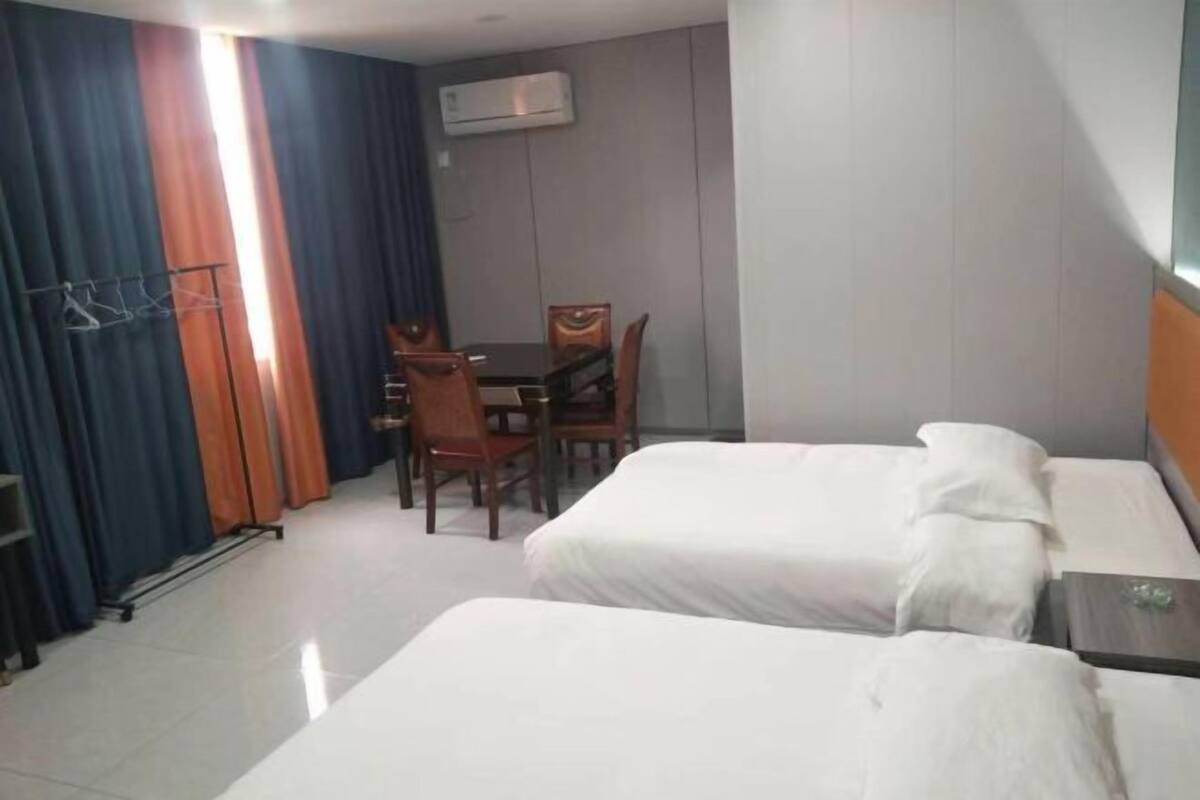 A hotel room with two beds, a dining table with chairs, and an air conditioning unit.
