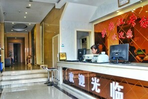 Mostrador de recepción de hotel con una computadora, un monitor, una silla y una escalera que conduce a otra zona.