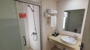 A modern bathroom with a glass-enclosed shower, a sink with a mirror, and neatly folded towels on a shelf.