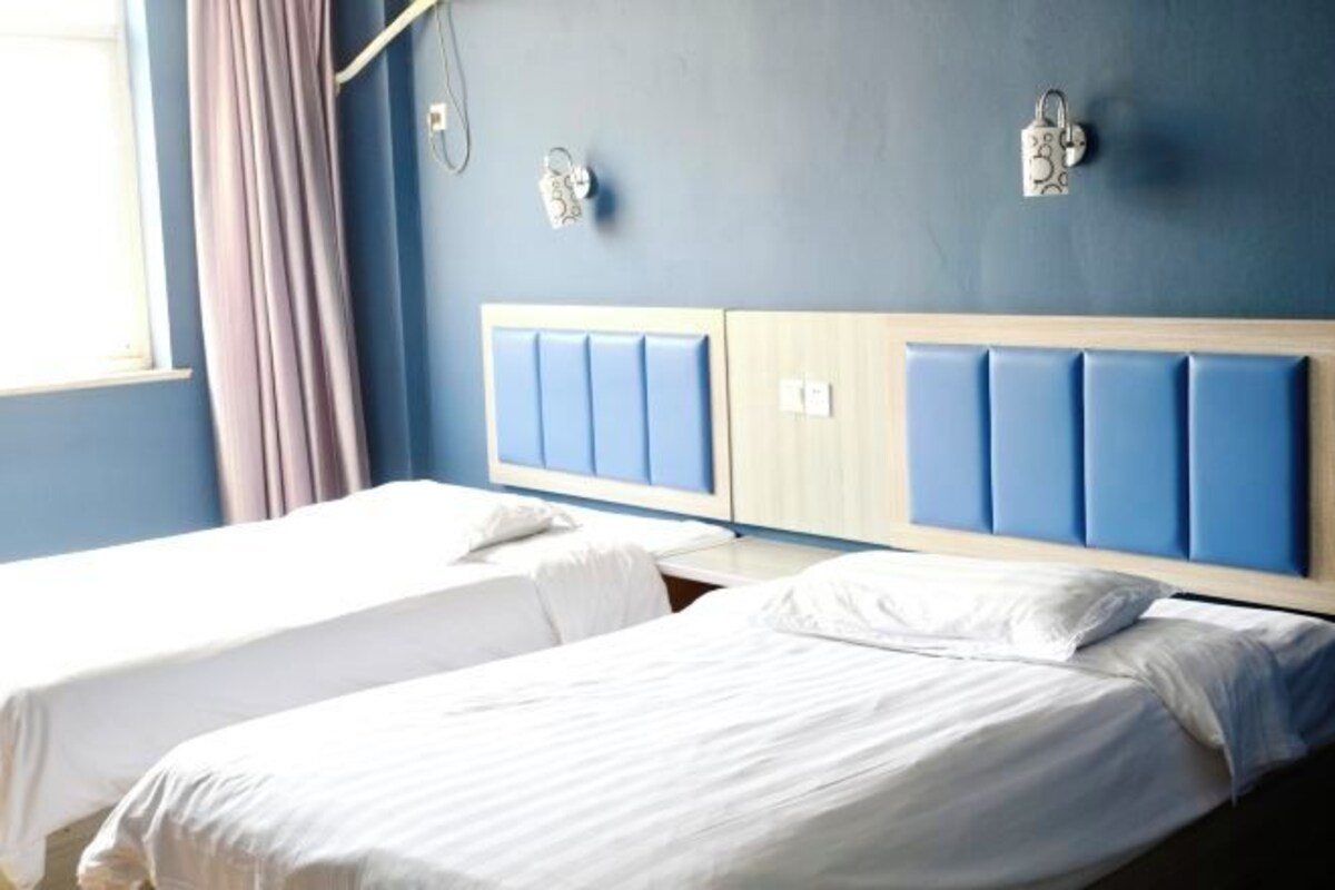 Habitación de hotel con dos camas, una pared azul y una ventana con cortinas.