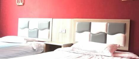 Habitación de hotel con dos camas, cada una con cabecera, mesita de noche y un inodoro instalado en la pared.