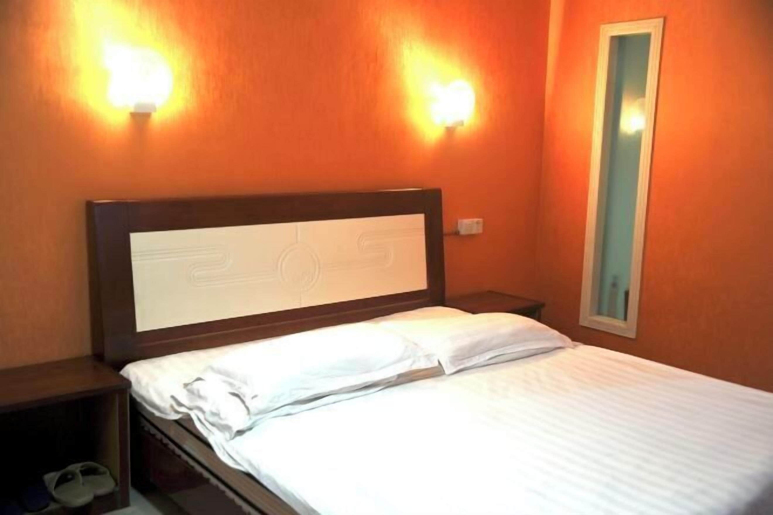 Una habitación de hotel con cama, mesitas de noche e iluminación en la pared.
