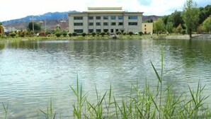 Un edificio de diseño arquitectónico moderno, situado junto a una masa de agua tranquila, con vegetación circundante y montañas al fondo.