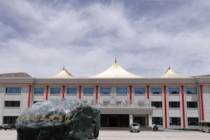 Un edificio con un gran monumento de piedra al frente, una serie de ventanas y un estilo arquitectónico distintivo con una cúpula central y dos cúpulas más pequeñas a cada lado.