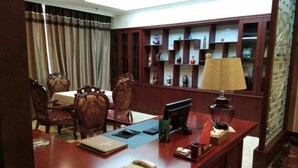 Habitación de hotel con un escritorio de madera, una computadora, una lámpara y una estantería con adornos.