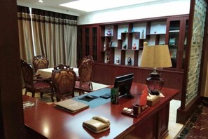 Ein Hotelzimmer mit Schreibtisch aus Holz, einem Computer, einer Lampe und einem Bücherregal mit Dekoration.