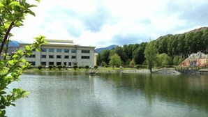 Un edificio de estilo arquitectónico moderno, un lago tranquilo y un telón de fondo montañoso.