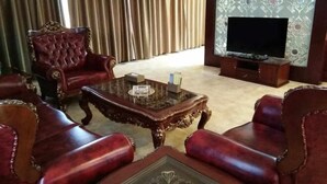 Ein Wohnzimmer mit Glastisch, roten Polsterstühlen, einem Fernseher und Vorhängen.