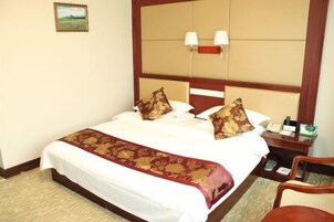 Habitación de hotel con una cama grande, una mesita de noche, una silla y una lámpara fijada a la pared.