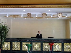 Ein Empfangsbereich mit Rezeptionist, Pflanze und dekorativen Wandverkleidungen.