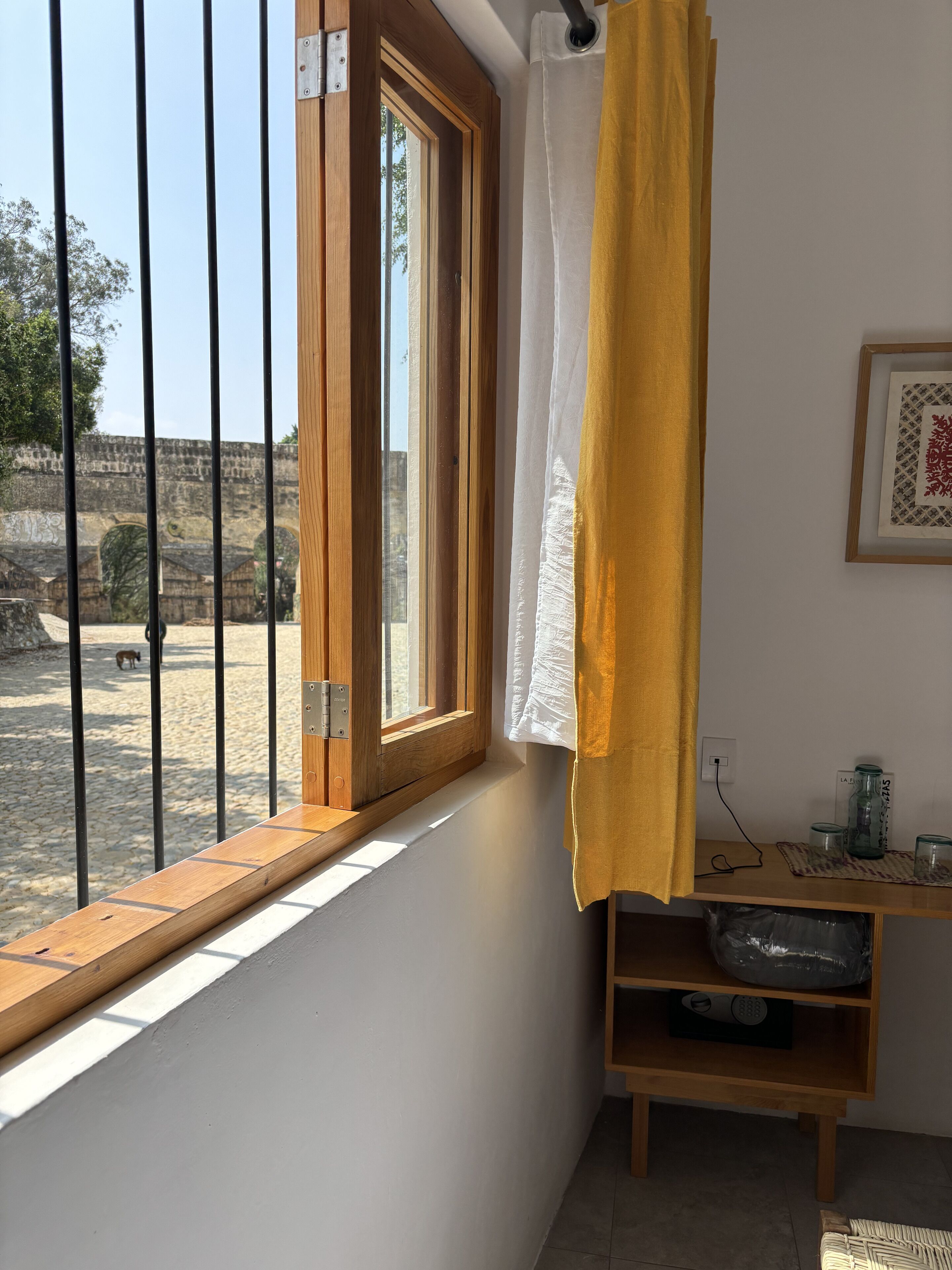 A room with a wooden window, a yellow curtain, and a shelf with jars and a speaker.