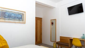 A bedroom with a bed, a desk, a chair, a TV, a mirror, and a framed artwork.