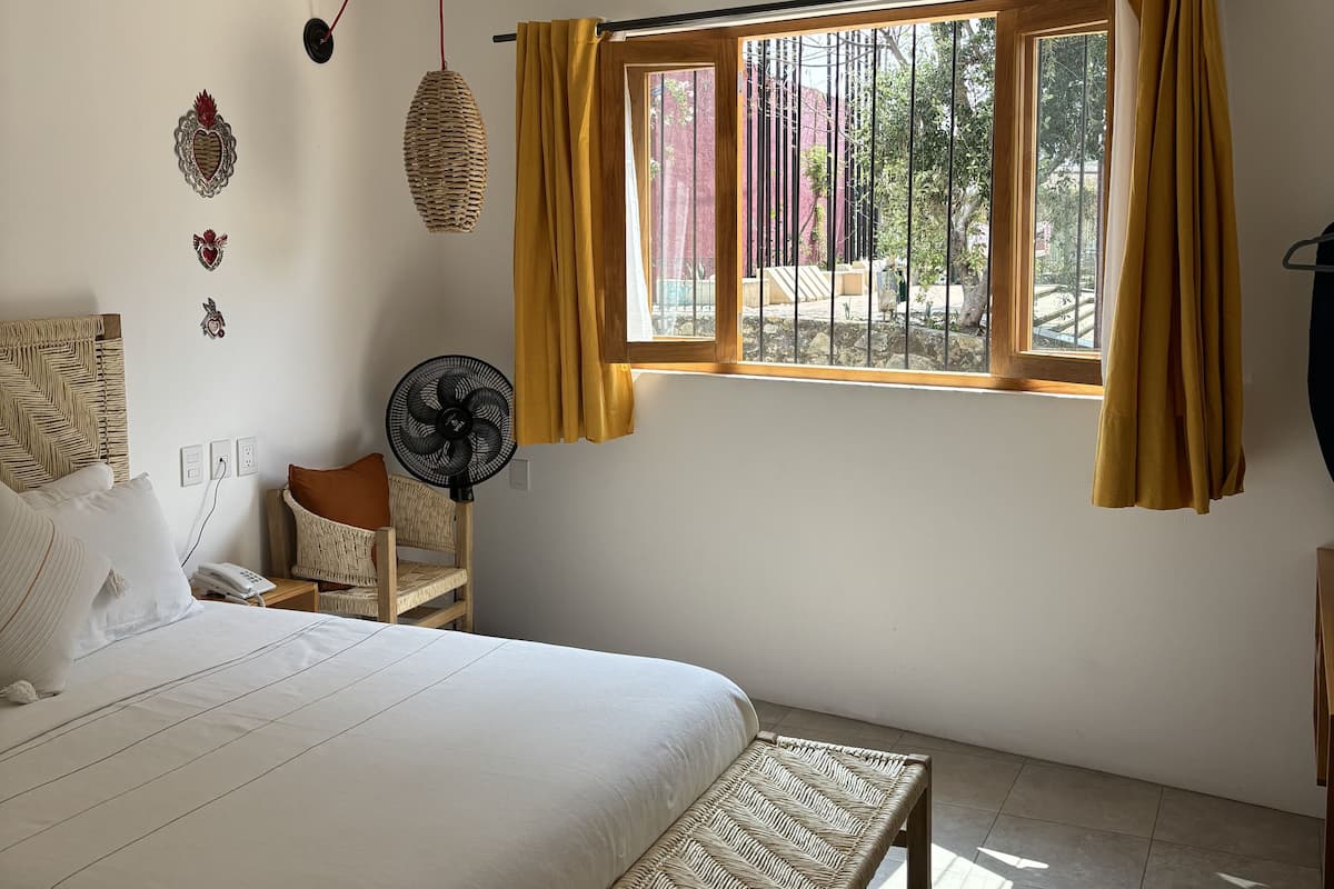 A bedroom with a bed, bedside table, chair, bench, window, and ceiling fan.