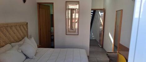 Habitación de hotel con una cama grande, cabecera de madera, un cuadro enmarcado en la pared, una silla amarilla y un espejo.
