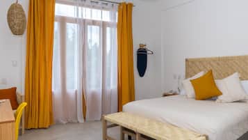 A bedroom with a bed, bench, curtains, and a wall-mounted hanger.