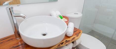 A bathroom with a white sink, wooden vanity, white toilet, and a glass shower enclosure.