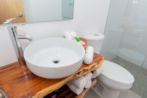 Um banheiro com pia branca, penteadeira de madeira, vaso sanitário branco e box de vidro.