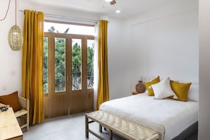 Quarto com cama, um banquinho, uma mesa e janela com cortinas.