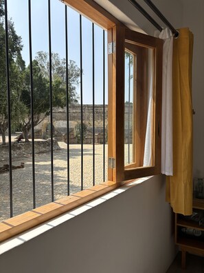 Quarto com uma grande janela que dá para um pátio com uma parede de pedra e árvores.