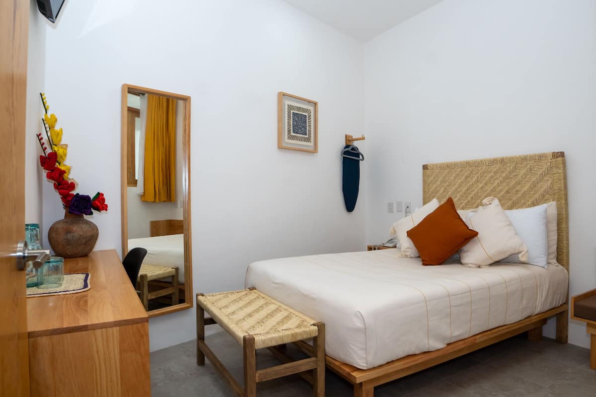 A bedroom with a wooden bed, a bedside table, a mirror, a framed picture, and a vase with flowers.