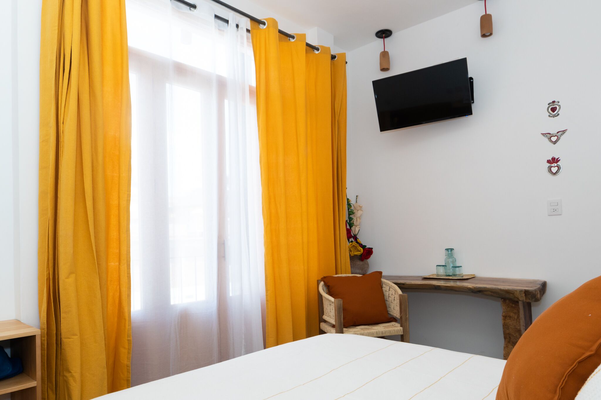 Ein Hotelzimmer mit einem Bett, einem Nachttisch aus Holz, einem Sessel, einem an der Wand befestigten Fernseher und gelben Vorhängen.