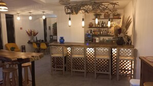 Angolo bar con bancone in legno, sedie in vimini e lampade a sospensione.